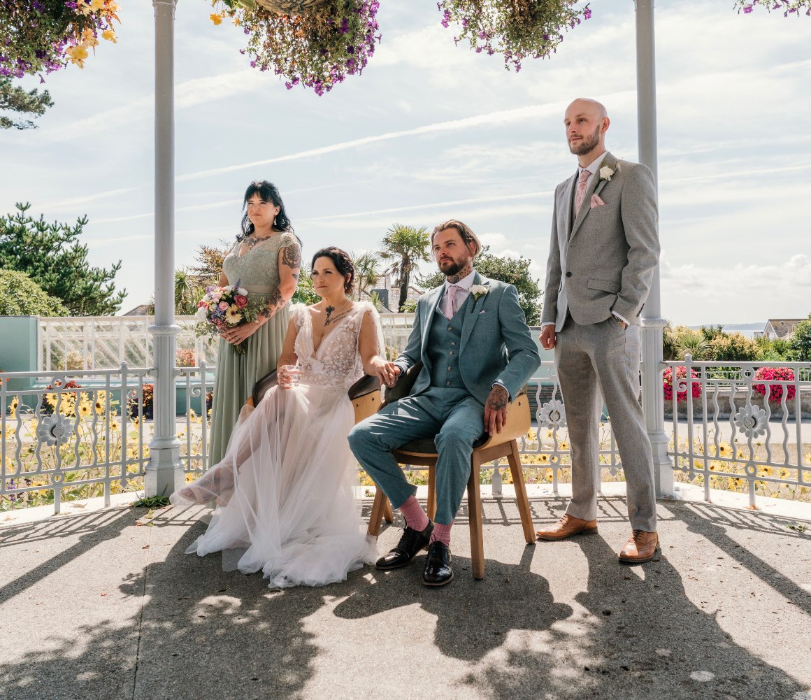 The wedding party under a flower-draped bandstand by the sea