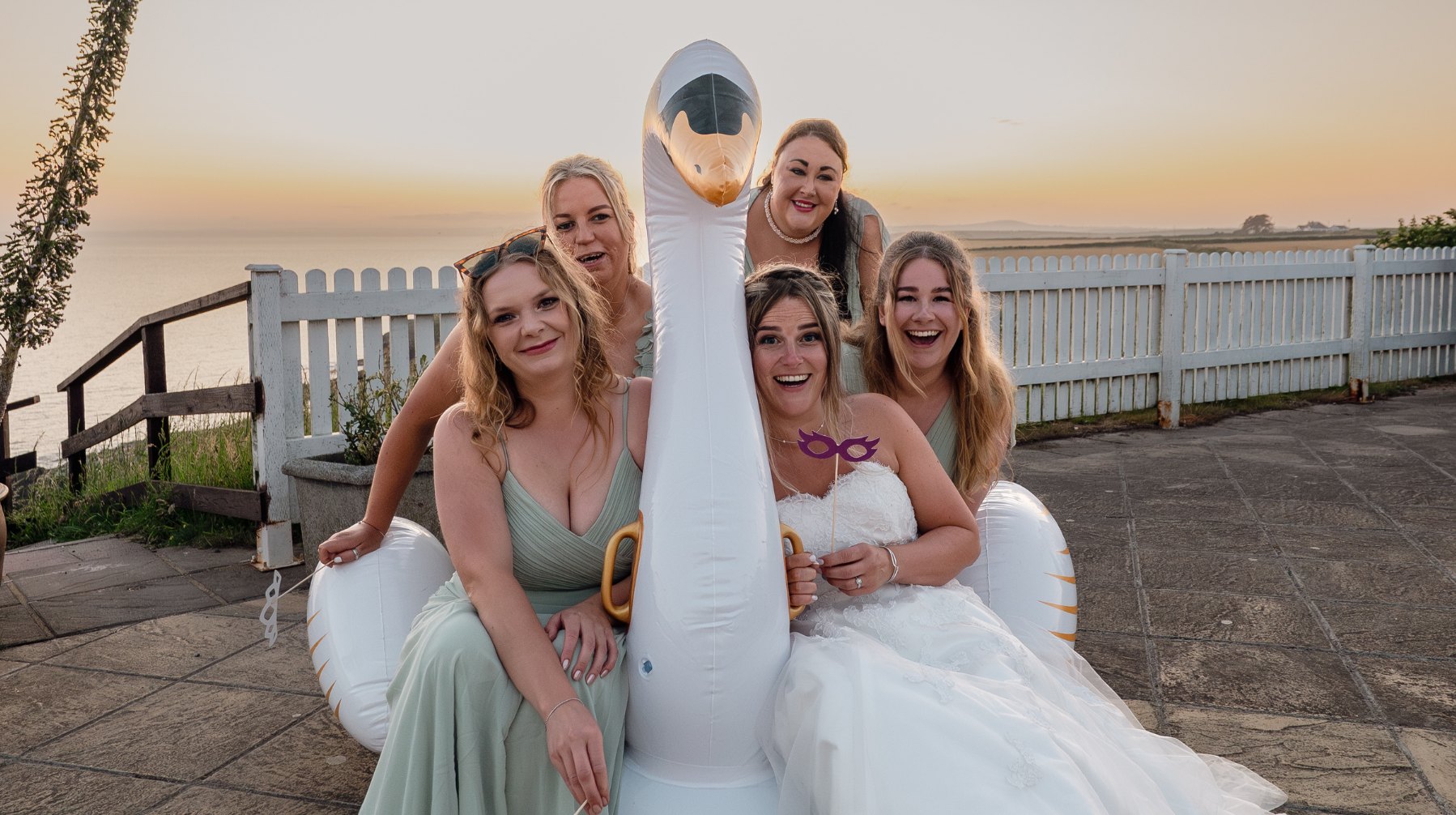 Bride and bridesmaids laughing on an inflatable swan at sunset