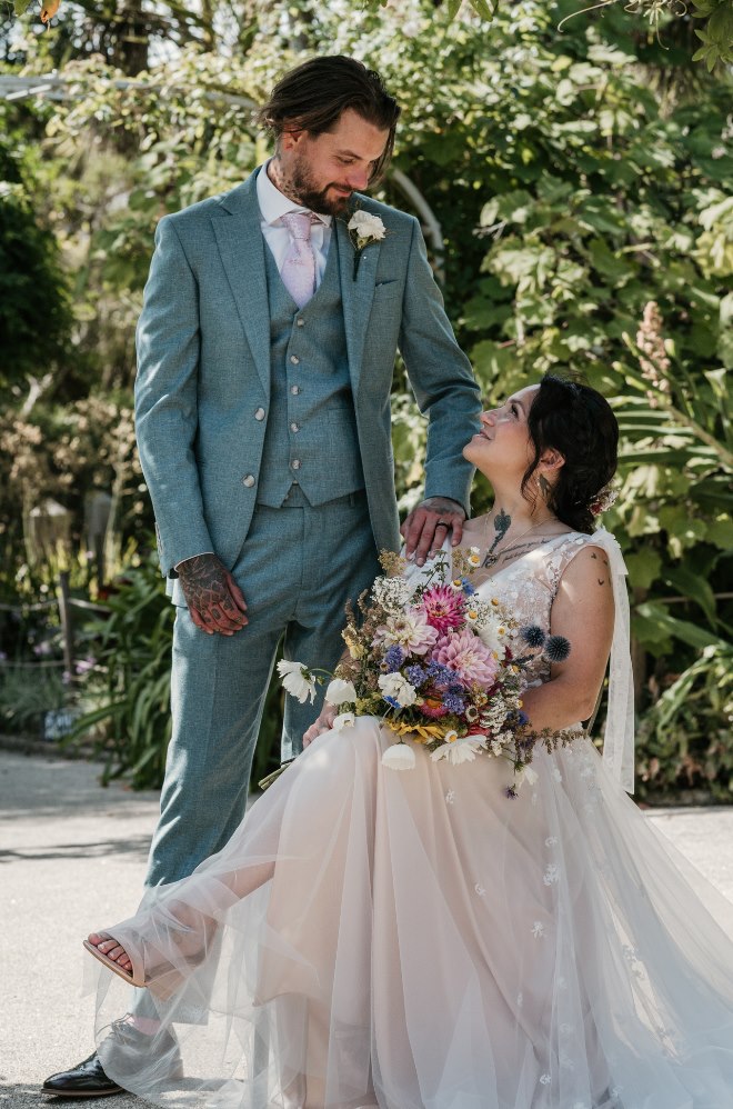 The groom smiling down at his seated bride holding her bouquet